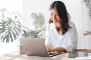 Young pretty asian housewife using laptop with household expenses and financial document on table, work at home concept.